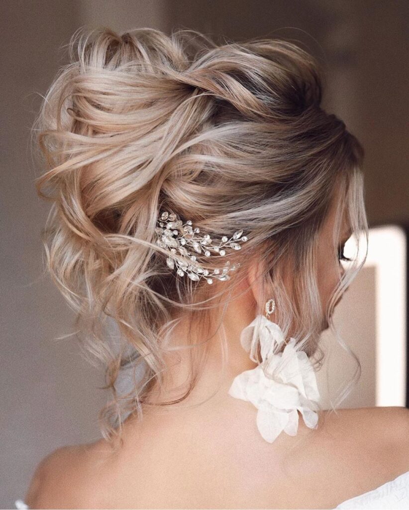 Back view of an ash-blonde balayage updo built from pinned curls with a crystal hair accessory.
