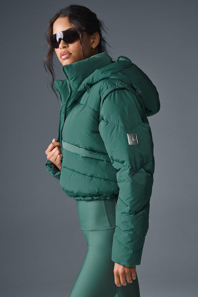 An emerald green cropped hooded puffer jacket worn over a tonal green sports top and matching green leggings.