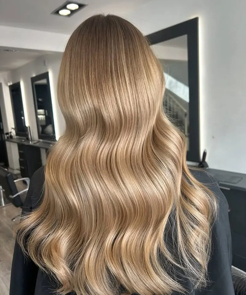Warm honey blonde balayage waves photographed from behind in a salon