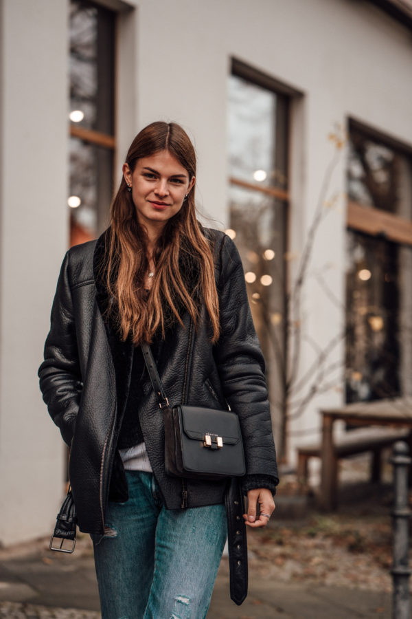 Woman wearing a black shearling jacket with distressed jeans and a crossbody bag in Berlin