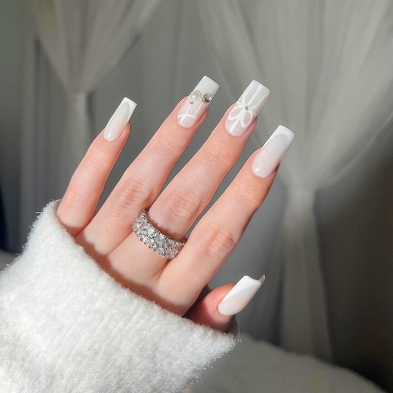 Long square white ombre nails with white hand-painted bows and pearl and gem accents
