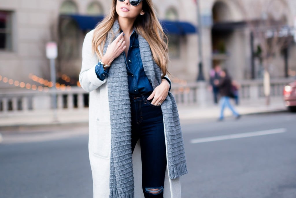Woman in a dark denim shirt and jeans with a long gray cardigan and scarf on a city street