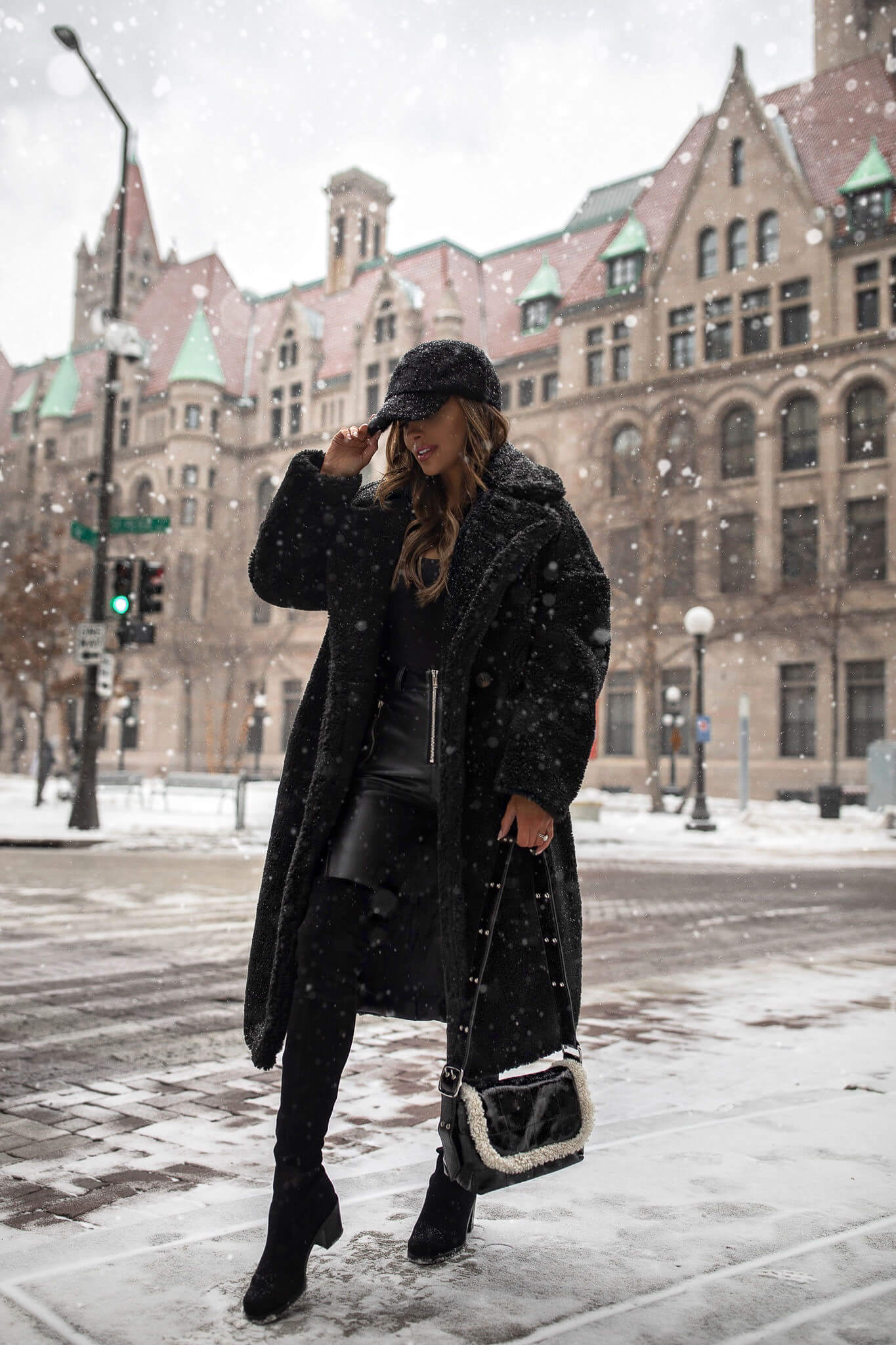 Woman in a long black teddy coat with black layers and over-the-knee boots standing in snow