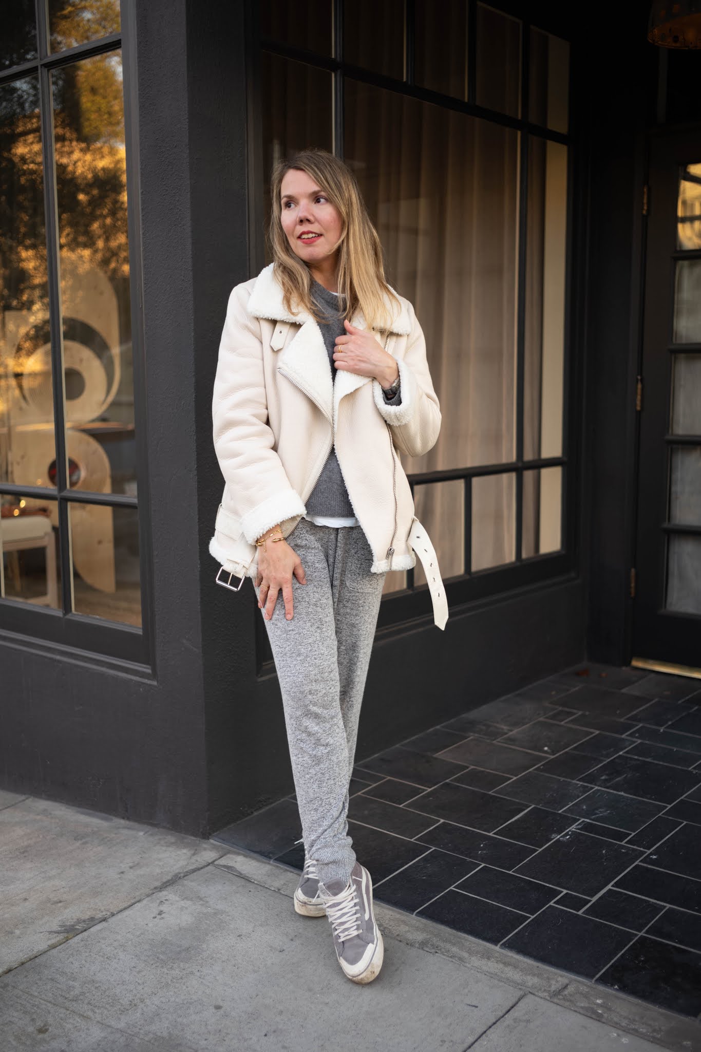 Woman in a cream shearling moto jacket with a grey sweater and grey sweatpants
