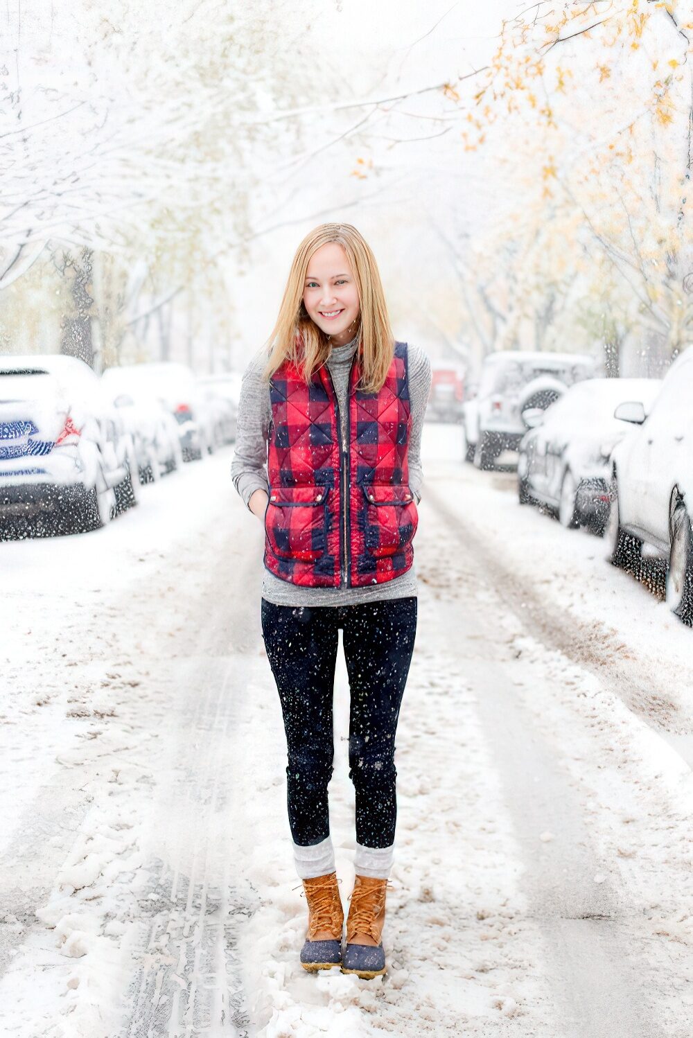 Woman in a red plaid puffer vest and duck boots standing on a snowy street