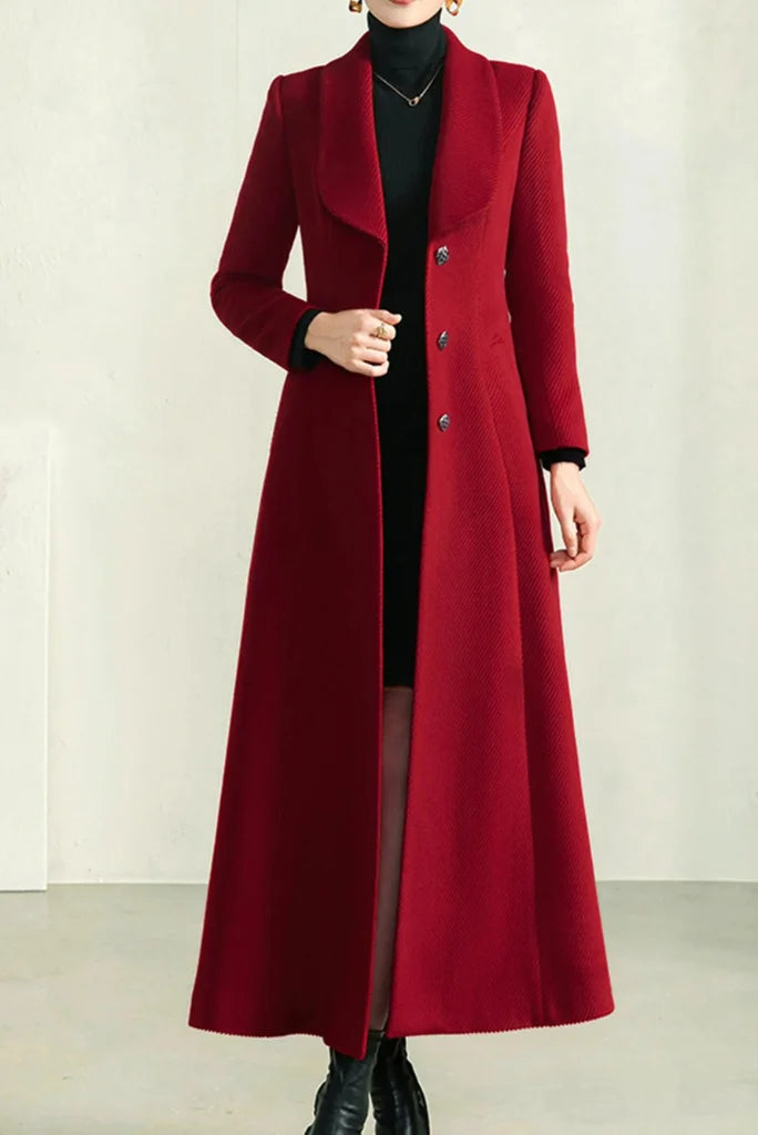 A full-length red wool coat worn over a black turtleneck dress with black boots and a black handbag.