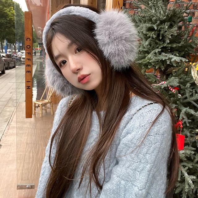 Woman in grey faux fur earmuffs and a pale blue fuzzy sweater