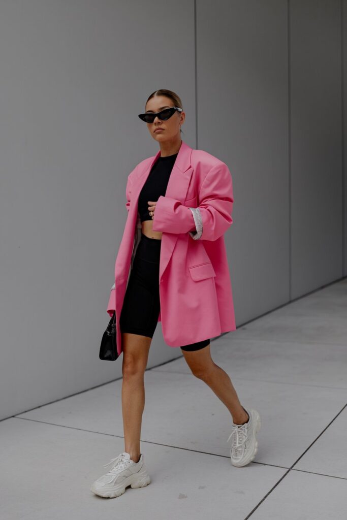 Woman in a hot-pink oversized blazer, black crop top, black bike shorts and chunky white sneakers