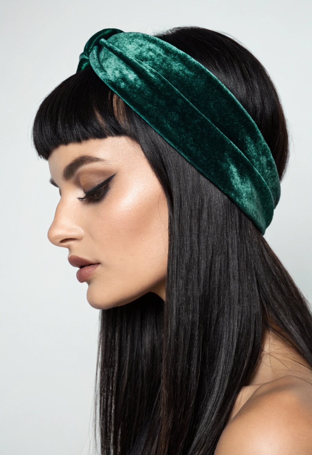 Woman with sleek black hair, blunt bangs, and an emerald green velvet headband