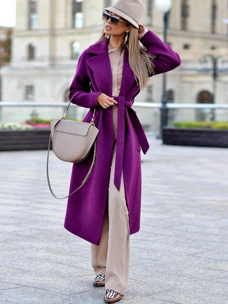 Woman in a purple wrap coat over beige outfit with beige hat and taupe bag