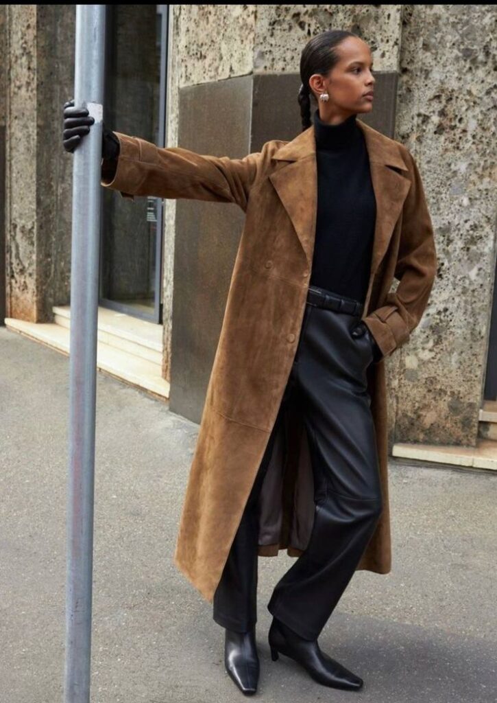 Woman in a long camel suede coat over a black turtleneck and black leather wide pants