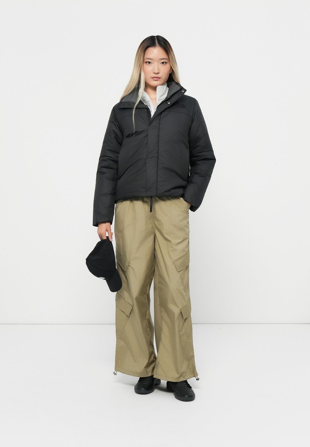 Woman in a cropped black puffer jacket, khaki cargo trousers, black sneakers and a black cap
