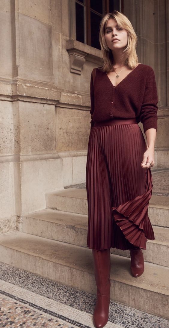 Woman in a burgundy knit cardigan with a pleated burgundy satin midi skirt and knee-high boots