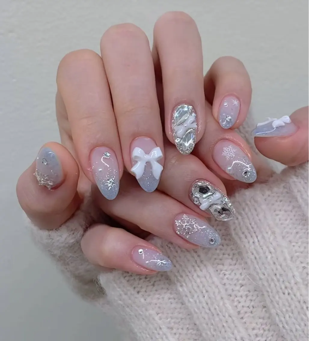 Icy blue glitter nails with white 3D bows and large crystal gem accents