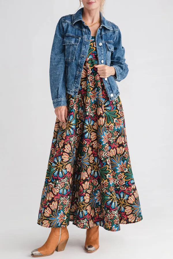 Woman wearing a colorful floral midi dress, denim jacket and tan ankle boots with metal toe caps