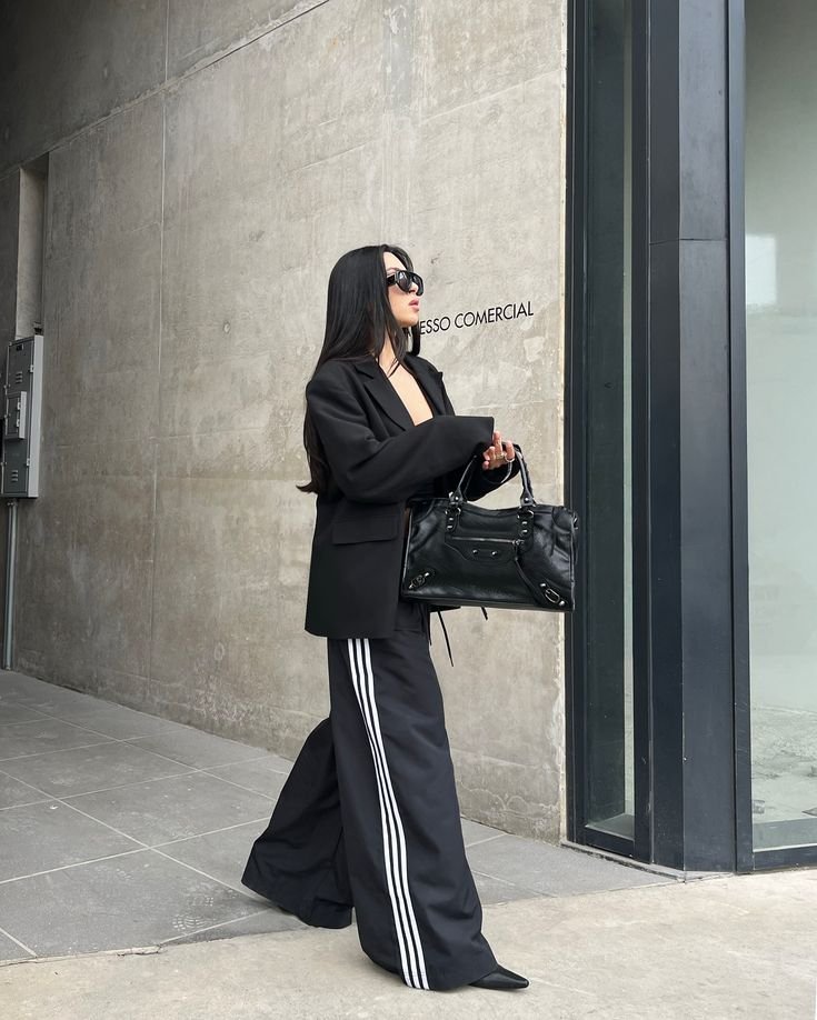 Woman in a black oversized blazer with black wide-leg track pants with white stripes