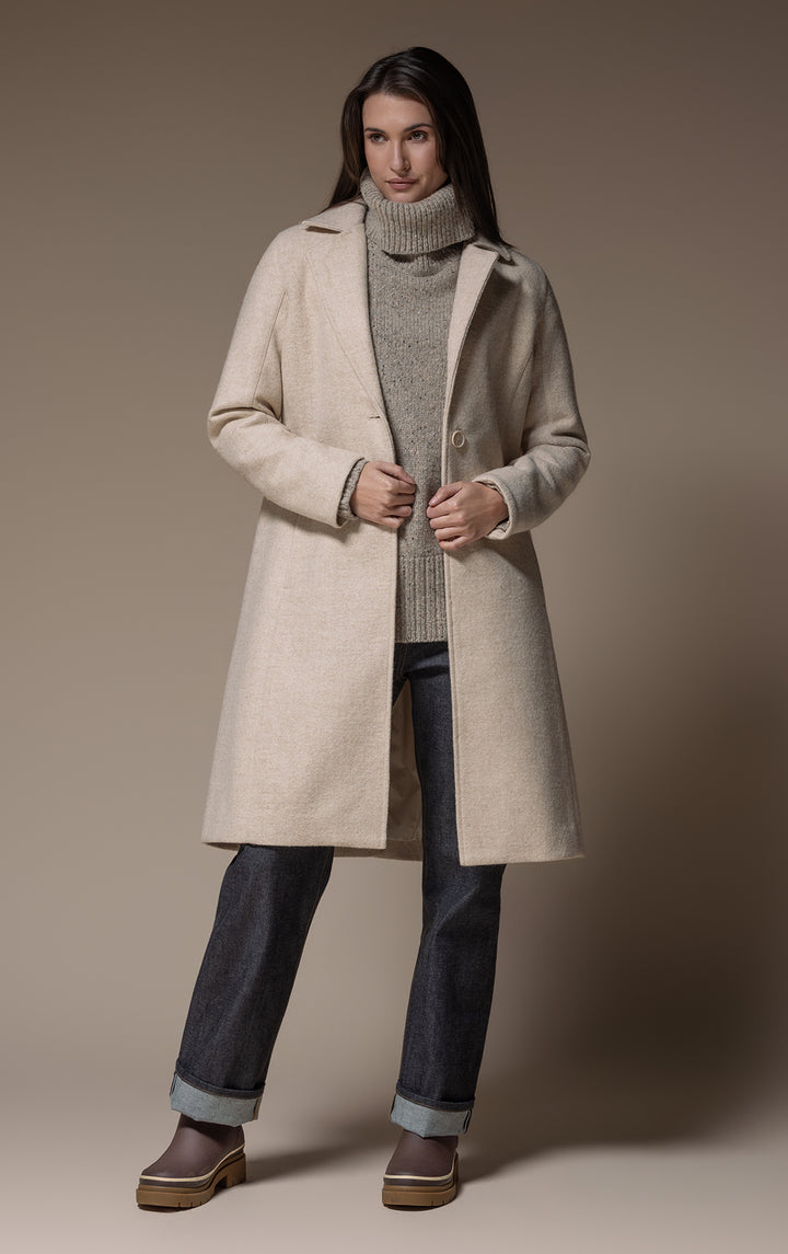 Woman wearing a cream wool coat, grey turtleneck, cuffed dark jeans and brown platform ankle boots
