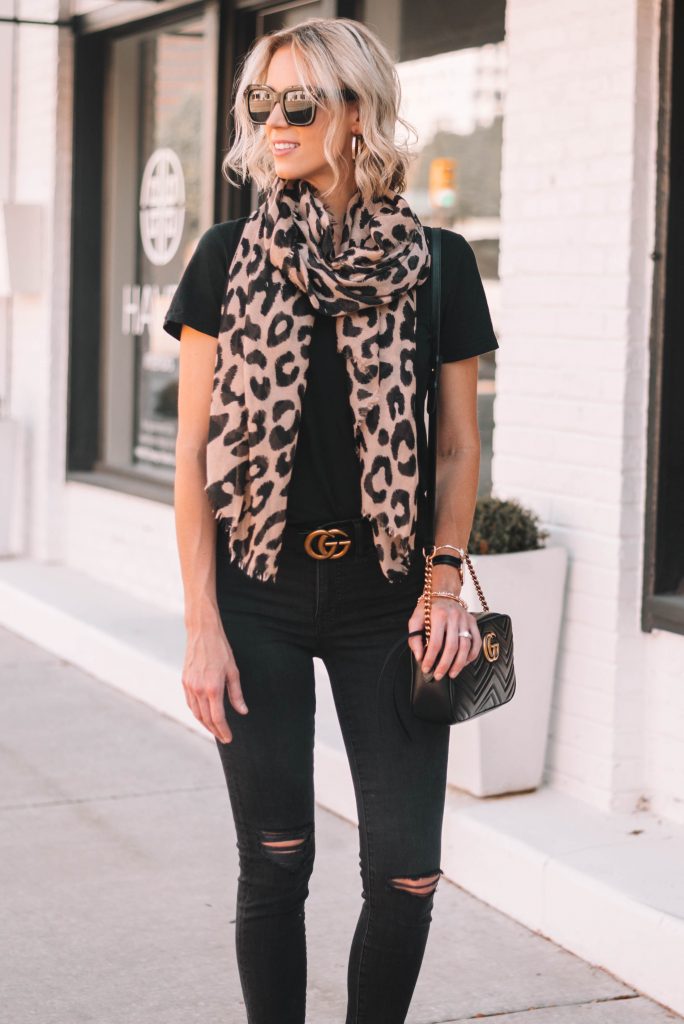 Woman styling a leopard print scarf with a black t-shirt, ripped black jeans and a gold buckle belt