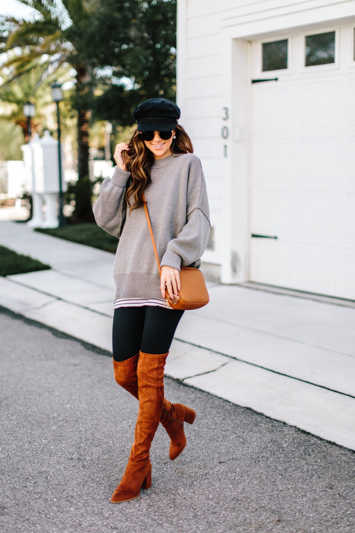 Woman in an oversized gray sweater, black leggings, cognac suede over-the-knee boots, newsboy cap and crossbody bag