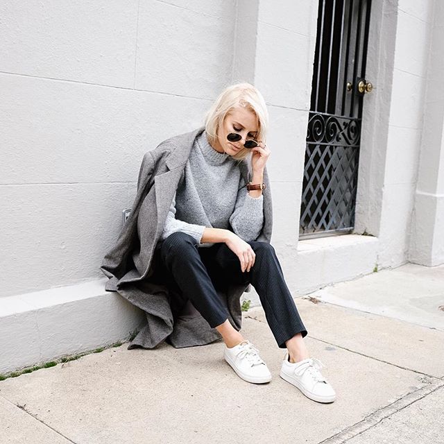 Woman in a grey coat draped over her shoulders with a grey sweatshirt, dark pants and white sneakers