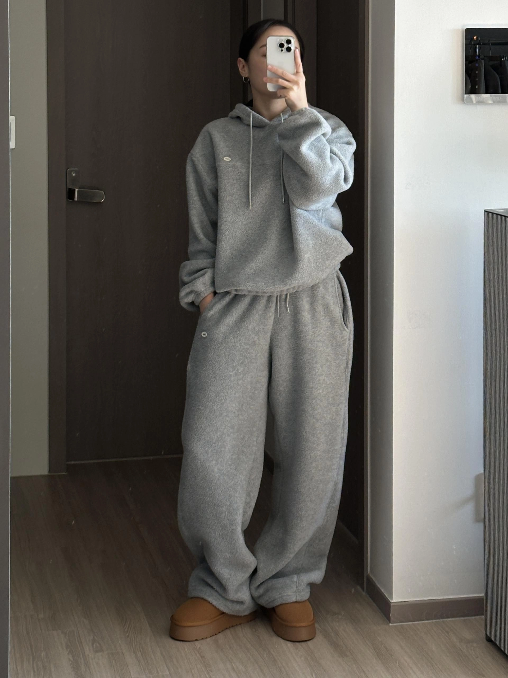 Woman taking a mirror selfie wearing a grey fleece hoodie, grey wide sweatpants and tan platform slippers