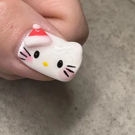 Close-up of a short square nail in white with a 3D sculpted Hello Kitty face wearing a Santa hat