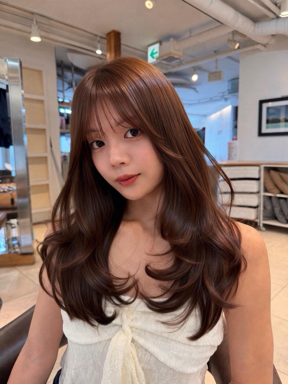 Warm chestnut brown long layered hair with face-framing fringe in a salon