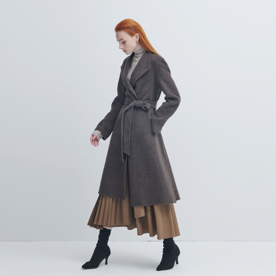 Woman wearing a belted grey wool wrap coat over a turtleneck with a camel pleated midi skirt and black ankle boots