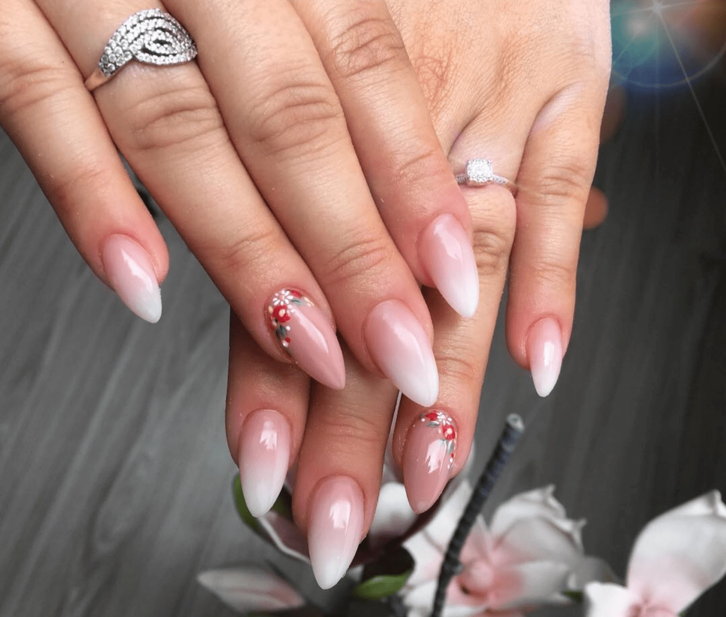 Medium almond nails with a baby boomer pink to white gradient and a small floral accent