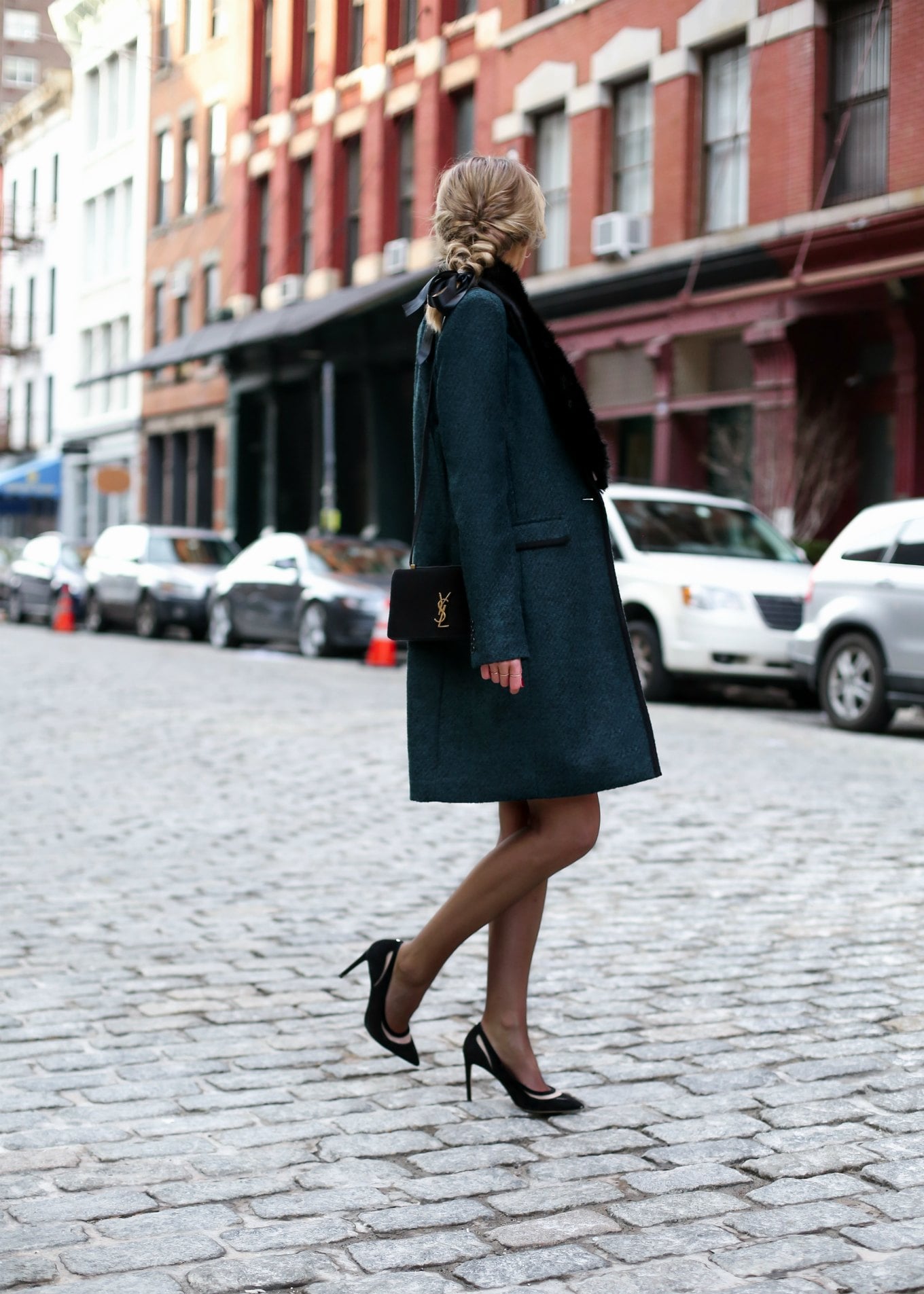Woman wearing an emerald green coat with a black faux-fur collar, black bag and heels