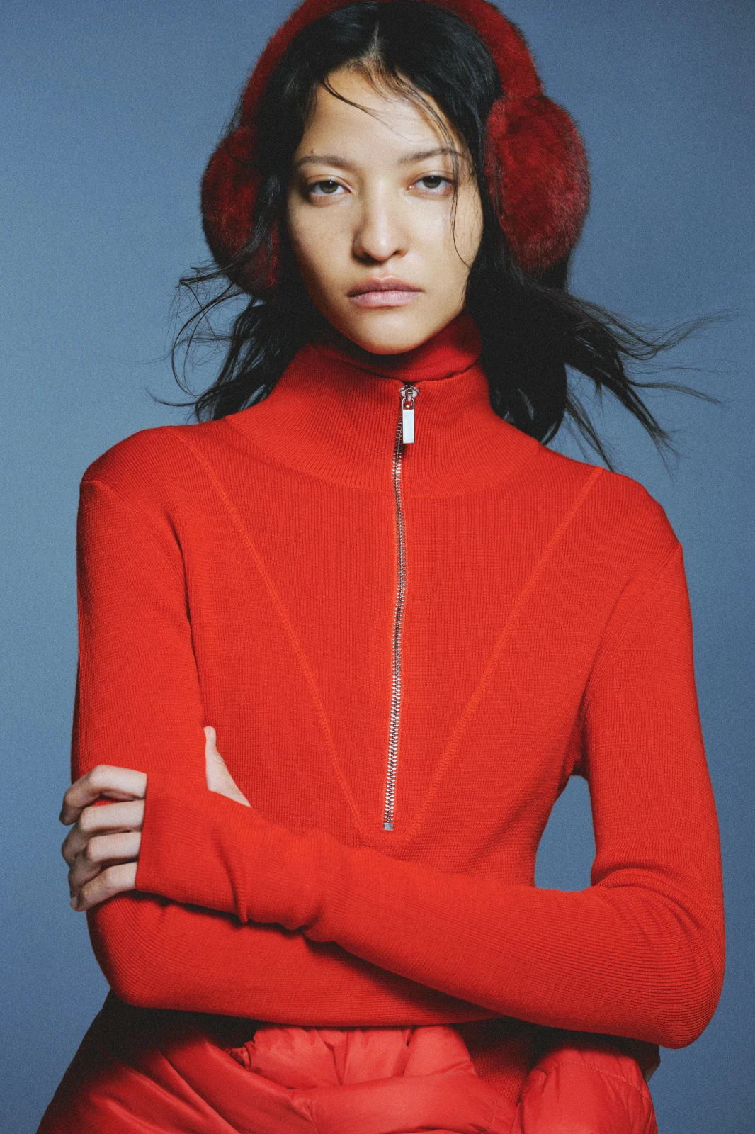 Editorial portrait of a woman wearing red faux fur earmuffs and a red turtleneck knit