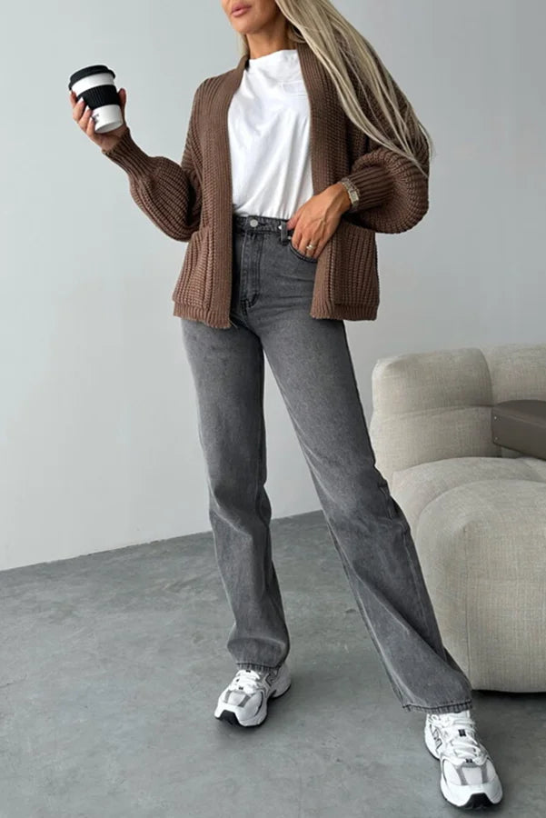 Woman wearing an open brown ribbed cardigan over a white t-shirt with grey wide-leg jeans and chunky sneakers
