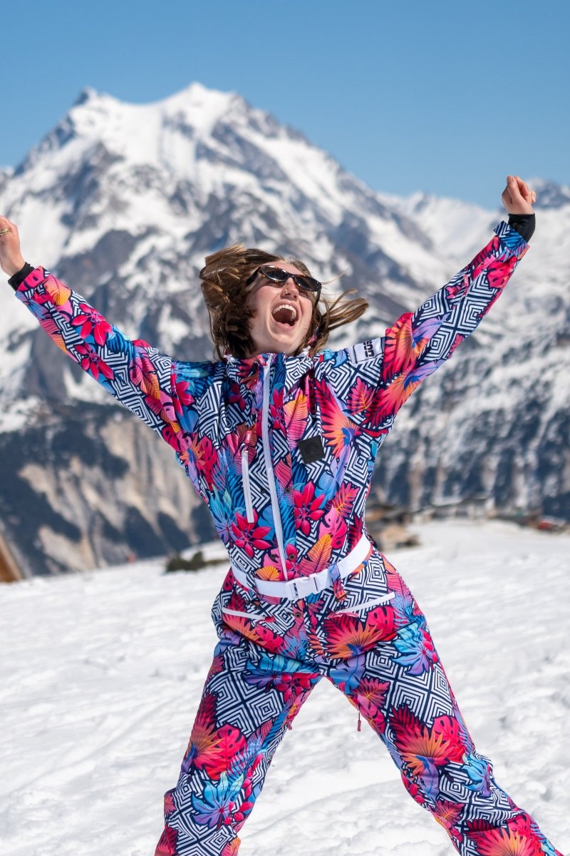 Woman in a colorful retro floral ski suit with arms raised on a snowy mountain