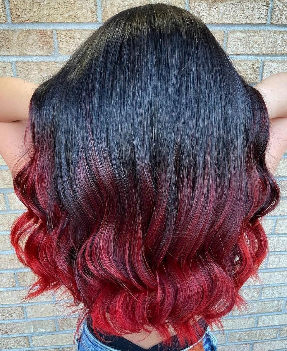 Back view of long wavy hair with black roots melting through burgundy into cherry-red ends