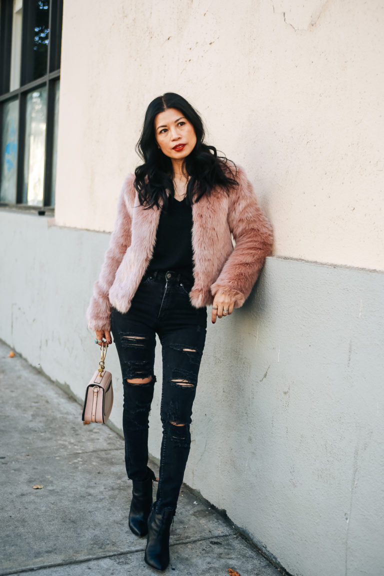 Woman in blush-pink cropped faux fur jacket, black ripped jeans, and heeled boots