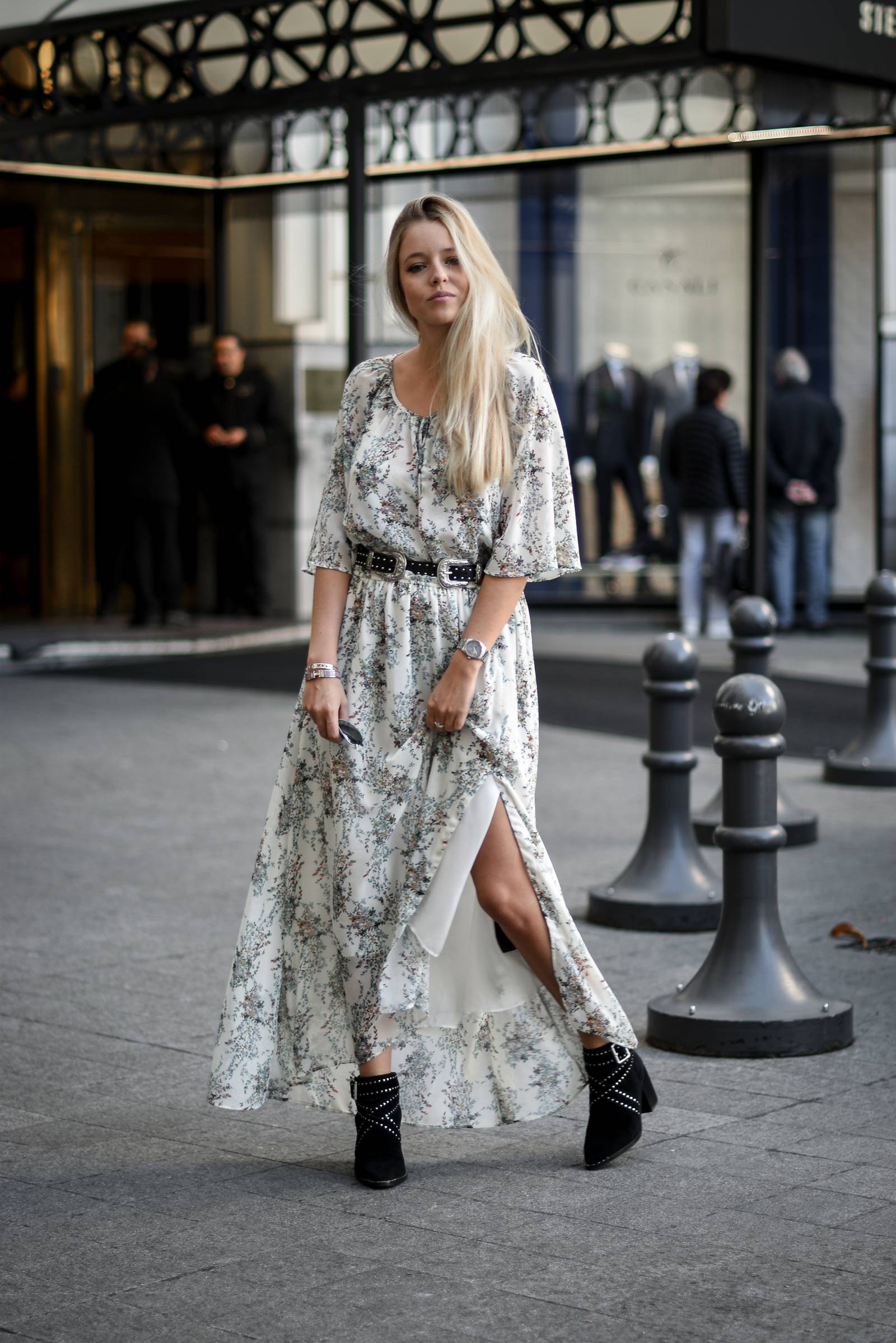 Woman in a white floral maxi dress with a western belt and black studded ankle boots