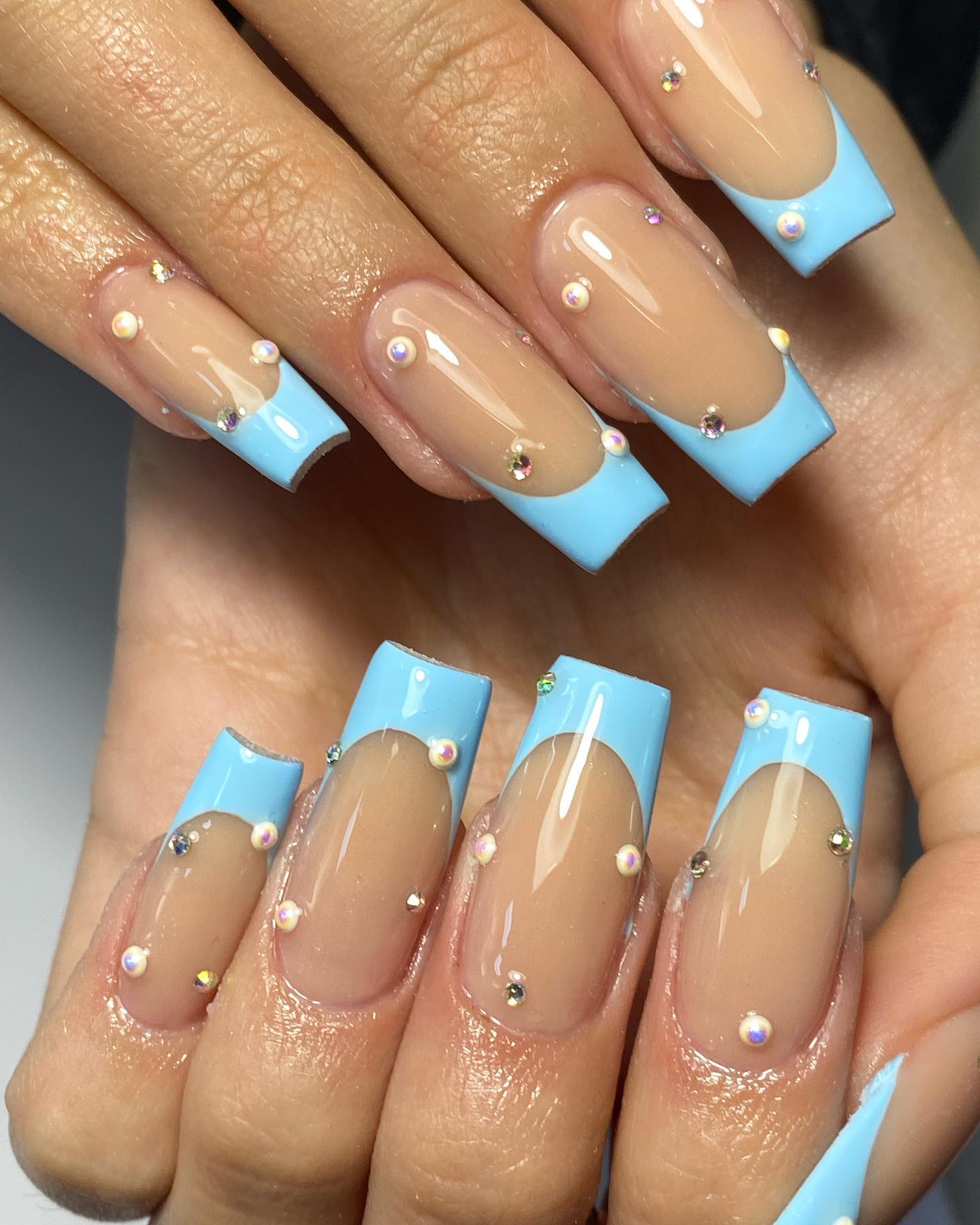 Blue French tip nails with a rhinestone accent on the ring finger