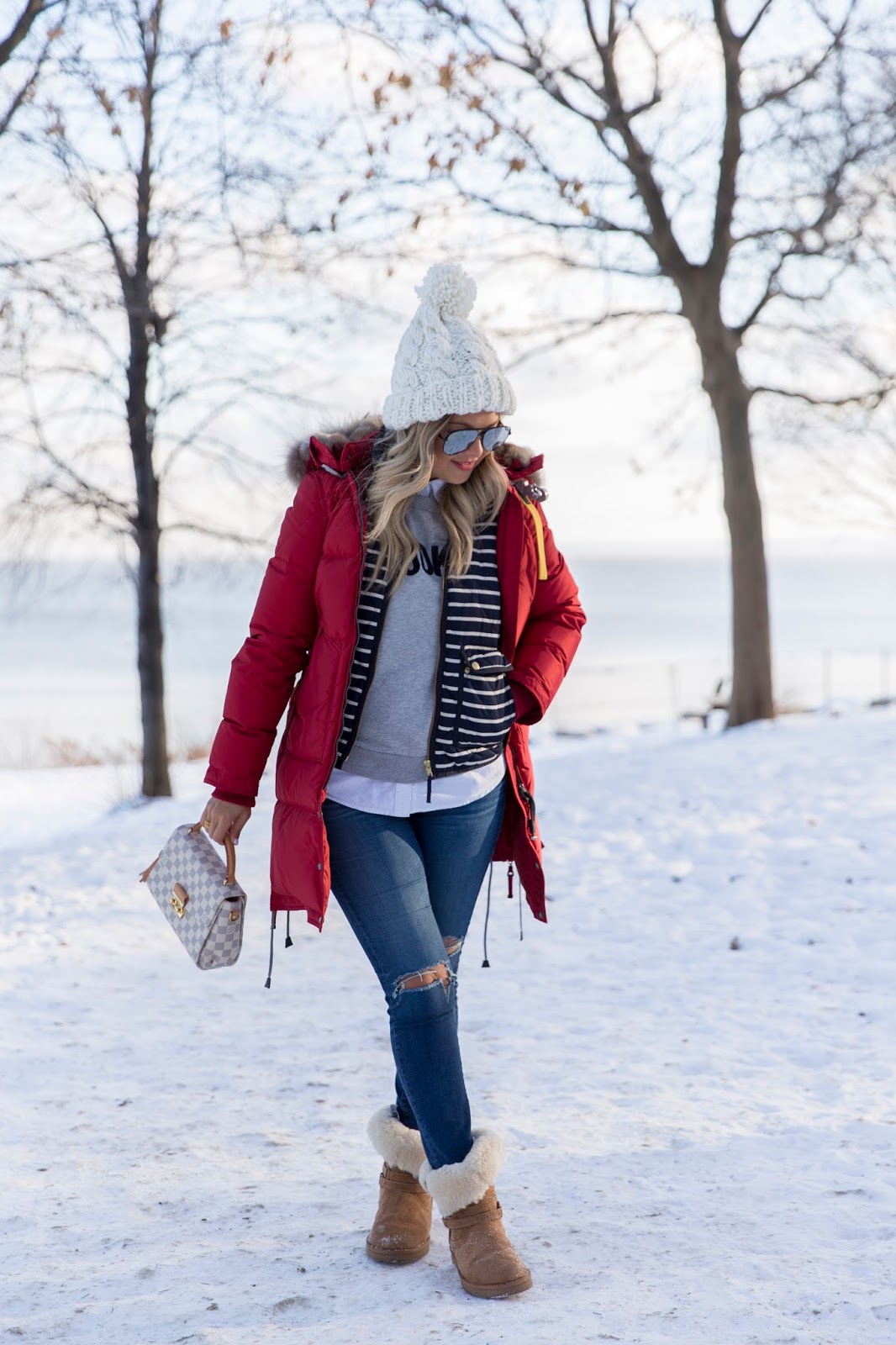 Woman in a red parka layered over a striped shirt and sweatshirt with shearling boots