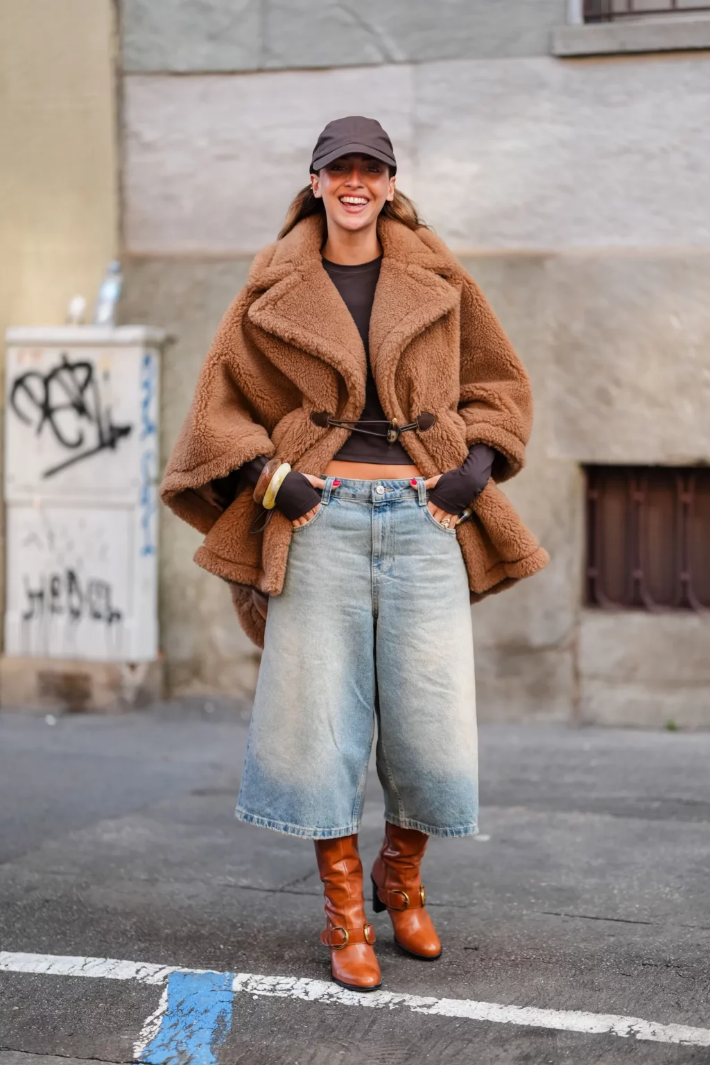 Woman in a cropped caramel teddy jacket with wide-leg jeans, tan buckle boots and a cap