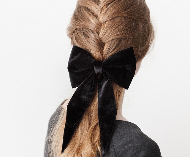 Back view of a blonde fishtail braid finished with a large black velvet bow