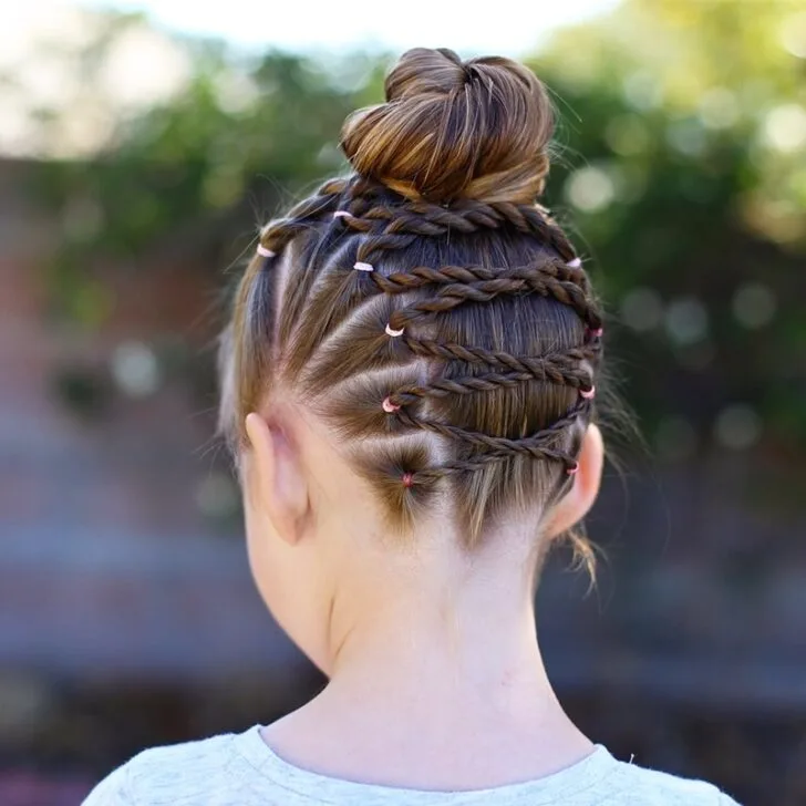 Back view of a young girl with crisscross braids gathered into a high bun (braided bun updo)