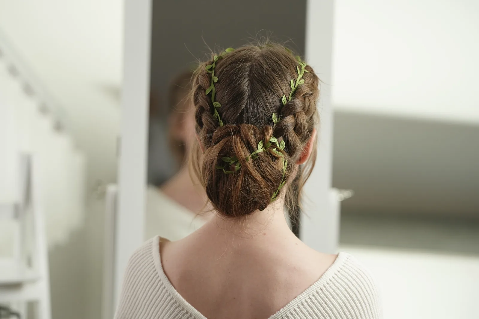 Back view of double Dutch braids woven from the front hairline into a low bun, dark brown hair.