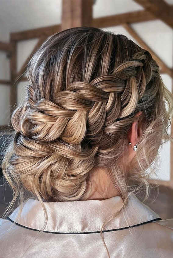 Chunky fishtail braid wrapped into a low bun on blonde balayage hair, back view.
