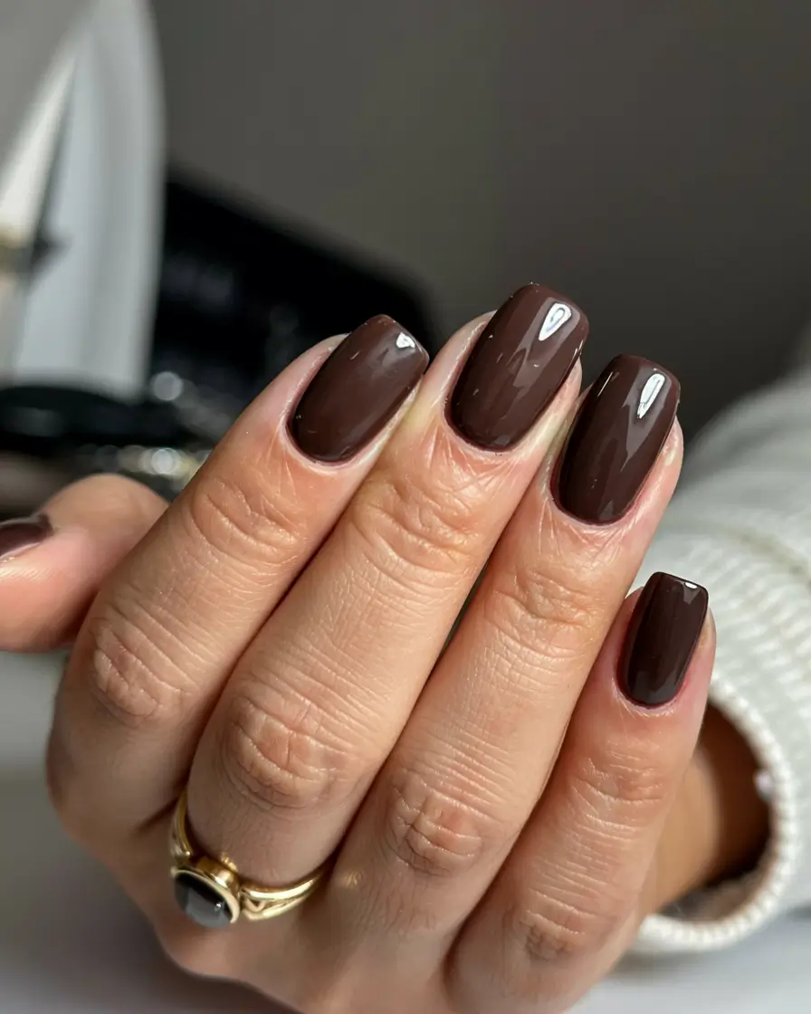 Short squoval nails in a warm chestnut reddish-brown crème with a glossy finish; real photography.