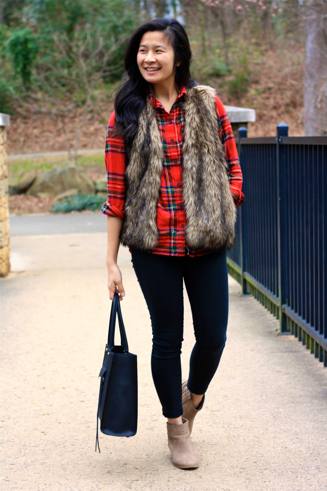 Woman wearing a faux-fur vest over a red plaid flannel shirt, black skinny jeans and taupe booties