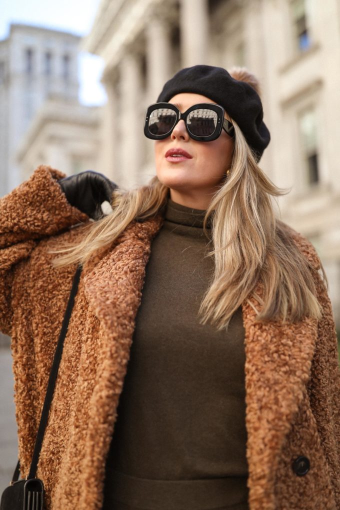 Woman wearing a caramel teddy coat with an olive turtleneck and a black beret