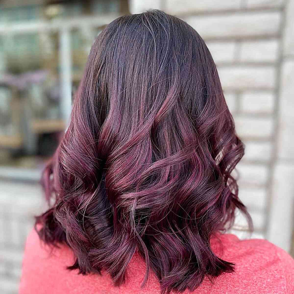 Burgundy balayage highlights on a shoulder-length wavy cut
