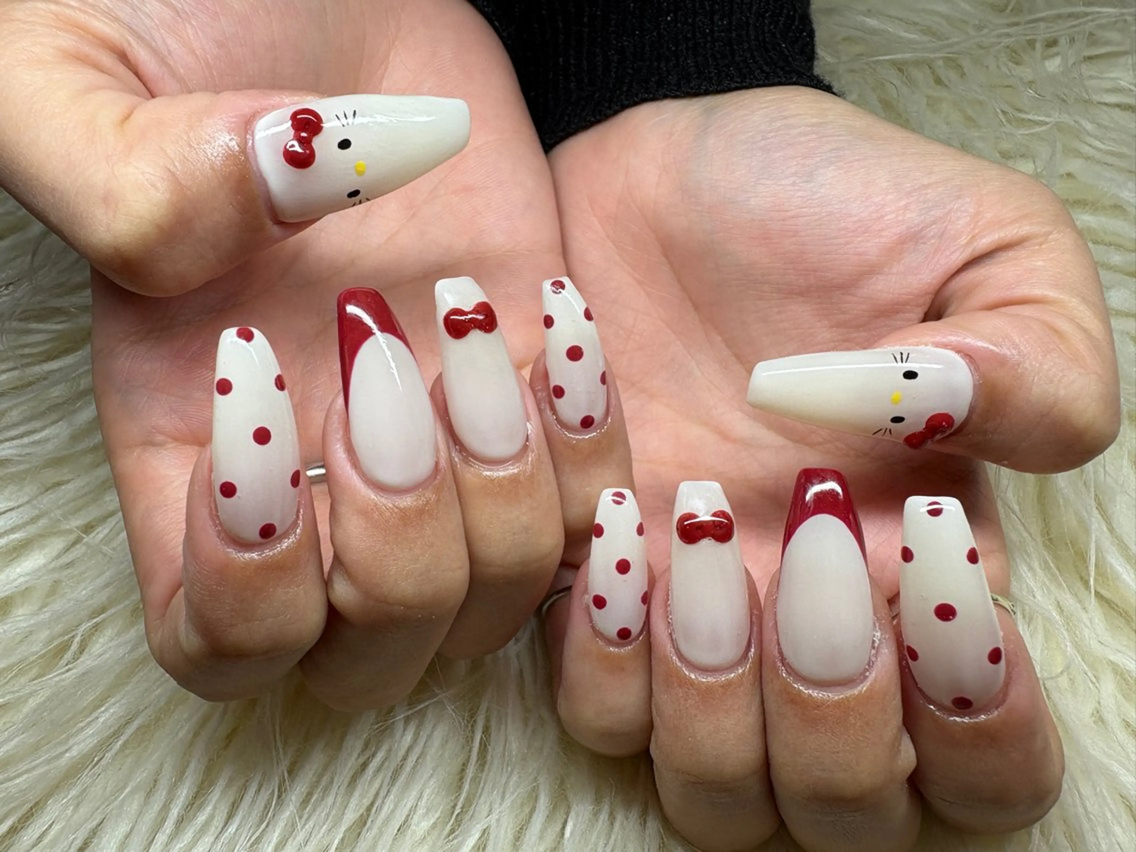 Long coffin nails in white with red polka dots, red French tips, red 3D bows and Hello Kitty faces