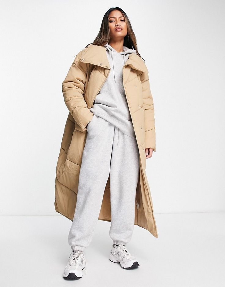 Woman wearing a beige long puffer coat over a matching grey sweat set with white sneakers