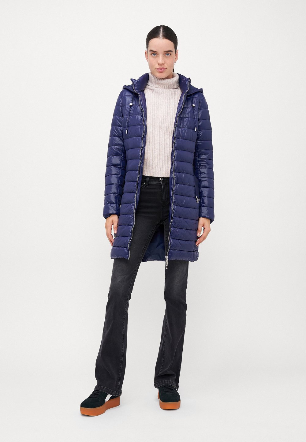 A navy mid-length quilted puffer with a hood, worn over a cream ribbed turtleneck, dark jeans and sneakers.